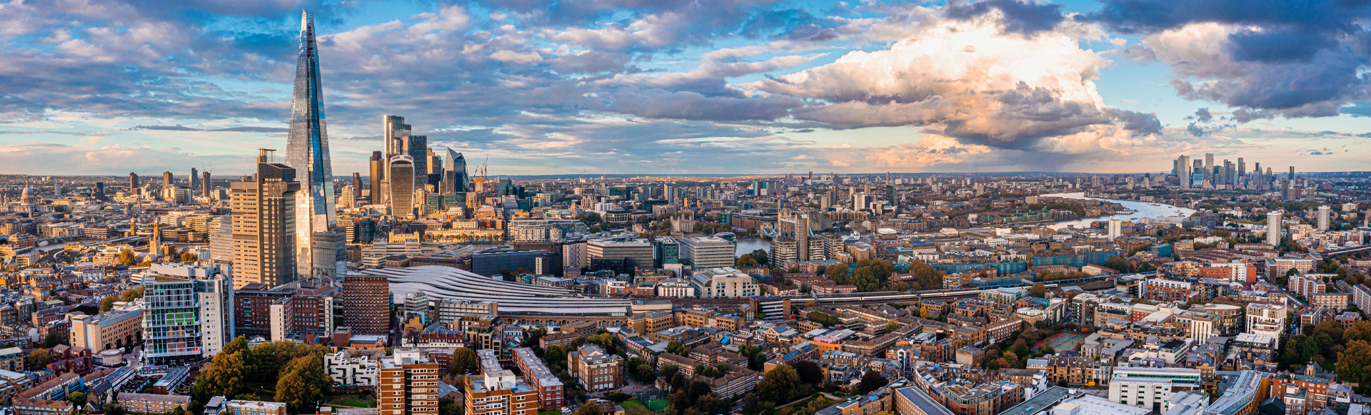 A daytime, wide-lens view of the London skyline with the Shard to the left and Canary Wharf in the background.