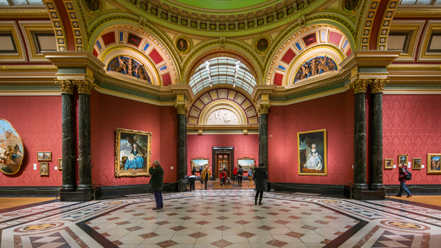 Interior of a classical, elegant art gallery with black and white marble floors and people looking at large paintings on the walls.