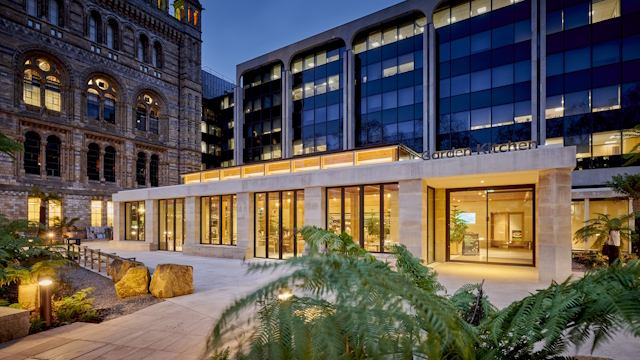 Garden Kitchen venue lit up in the evening with yellow light, with Natural History Museum building in the background to the left, modern building to the right.