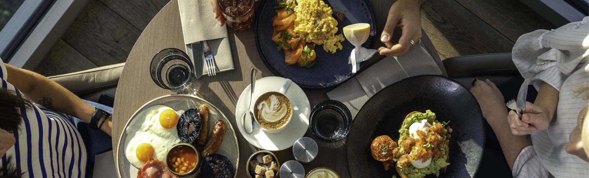Three brunch plates, coffee and drinks placed on a wooden table, photographed from above.