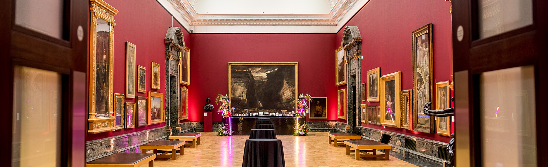 A shot of Tate Britain's Gallery 9 with multiple paintings hanging on the red walls.