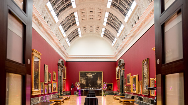 A shot of Tate Britain's Gallery 9 with multiple paintings hanging on the red walls.