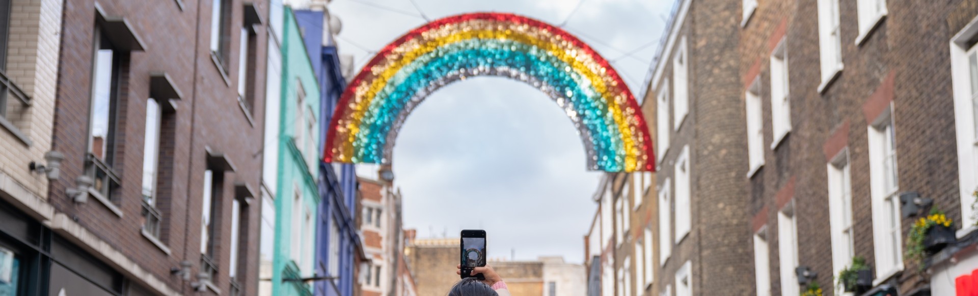 A glittery rainbow hanging over Carnaby Street in London on a cloudy day.