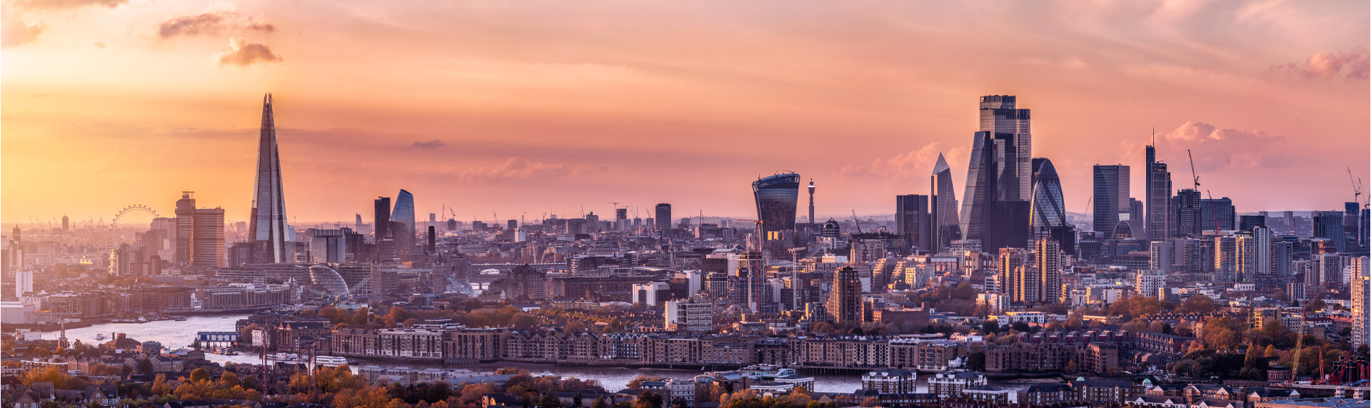 An evening view of the London skyline with the Shard and the City skyscrapers visible in the background and the river Thames in the foreground.