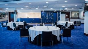 Round table arrangements with white table cloths on blue carpet in the Chelsea FC event venue.