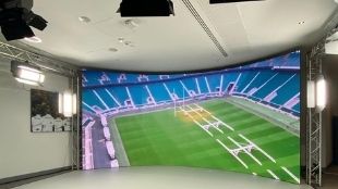 A big wall-to-wall screen inside a studio showing the Twickenham Stadium ground from above.