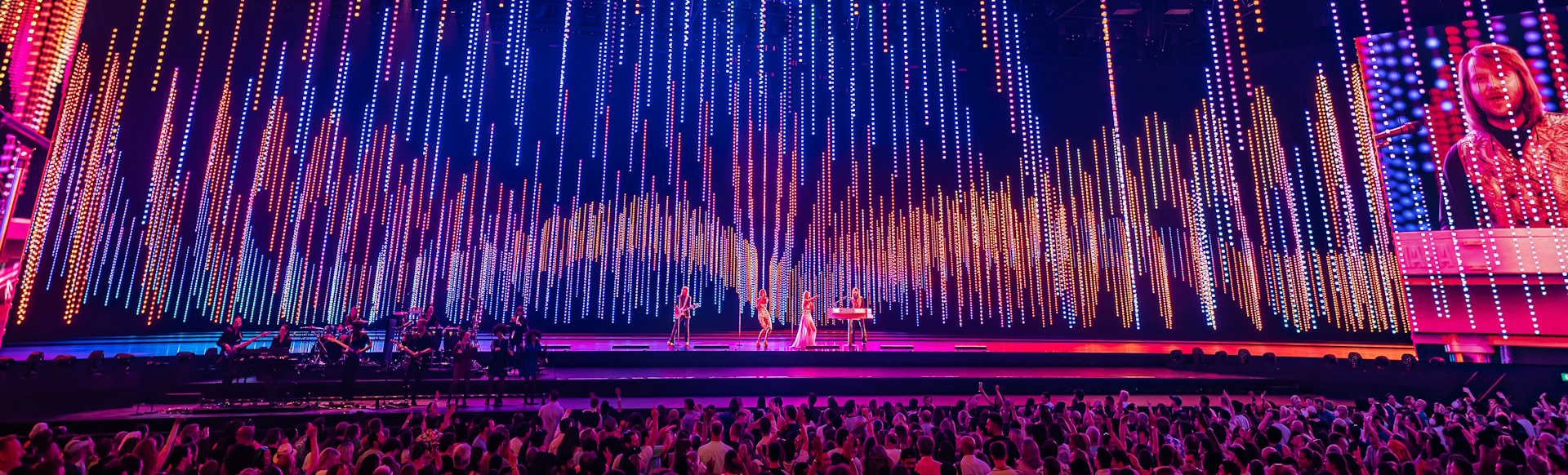 ABBA Arena stage lit up in pink, orange and purple lights during a live performance of ABBA Voyage in London.