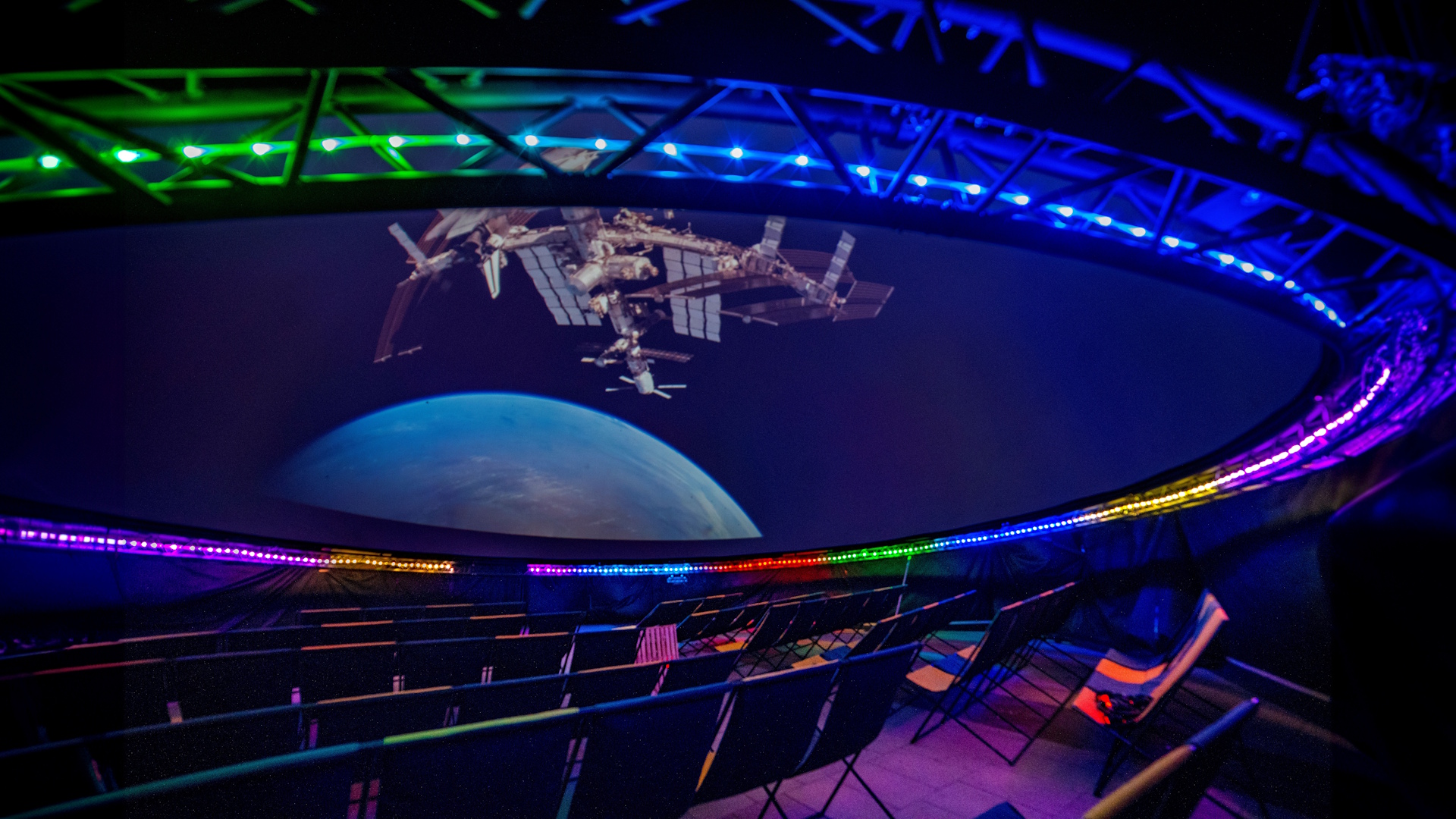 A show inside a planetarium lit in various colours with planet Earth and a satellite projected onto the screen on the ceiling.