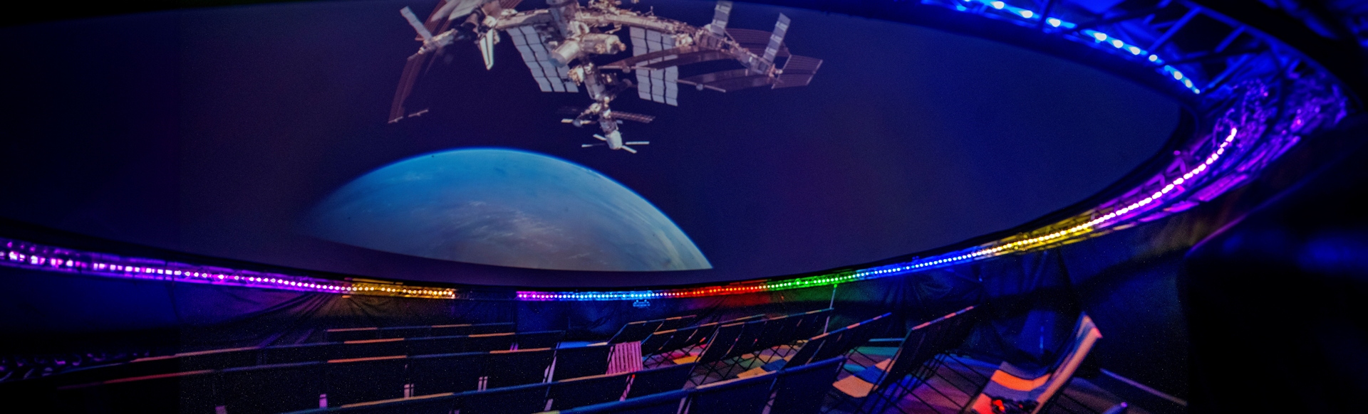 A show inside a planetarium lit in various colours with planet Earth and a satellite projected onto the screen on the ceiling.