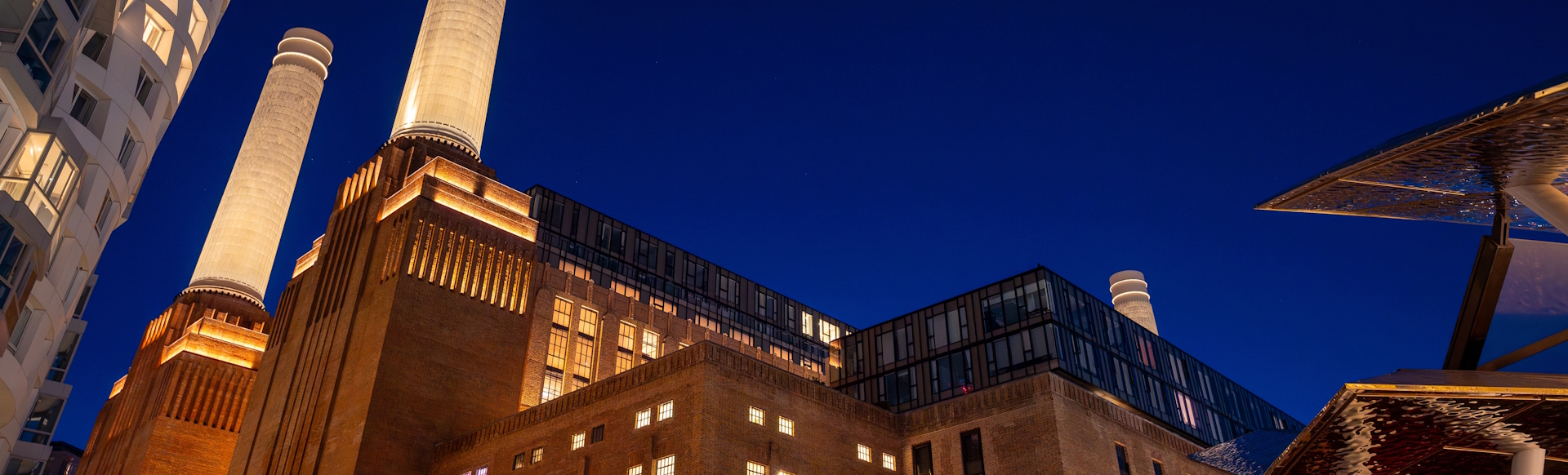 Battersea Power Station lit up at night with dark blue sky.