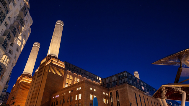 Battersea Power Station lit up at night with dark blue sky.