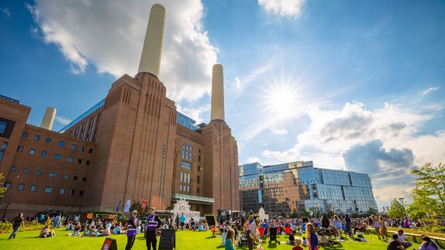 Battersea Power Station offers plenty of fantastic experiences and event spaces. Credit: Charlie Round-Turner. Image courtesy of Battersea Power Station. Battersea Power Station chimneys with people sitting on the grass in front and blue sky with sunshine.