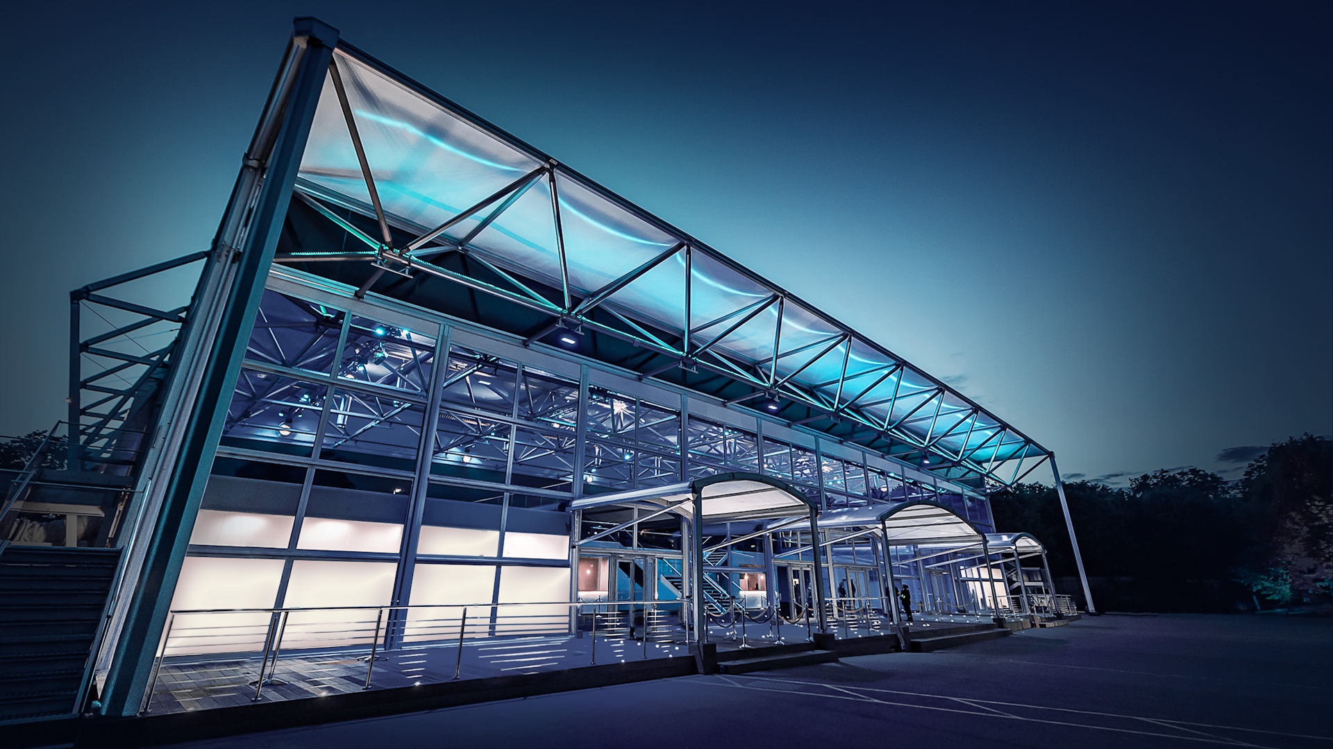 Steel and glass structure of Evolution London events venue at night with blue and white lights.