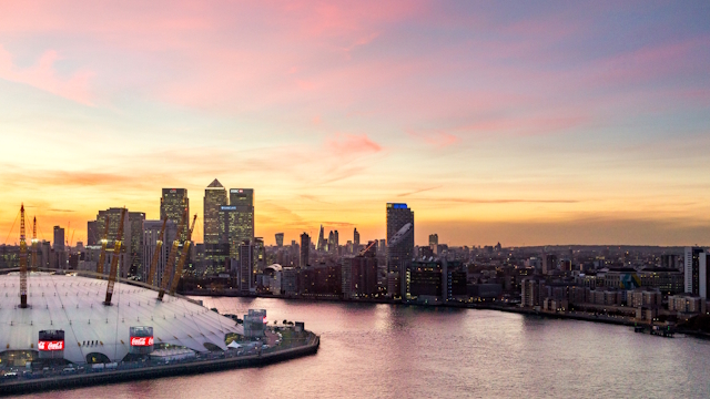 View of Canary Wharf skyline at sunset with The O2 entertainment venue and the river Thames in the foreground.