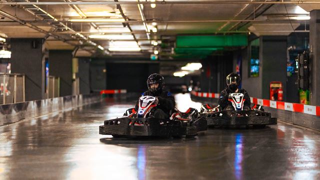 Experience K1 Speed in Canary Wharf. Credit: K1 Speed. Image courtesy of K1 Speed. Two racers dressed in black enjoying an indoor go-karting track.