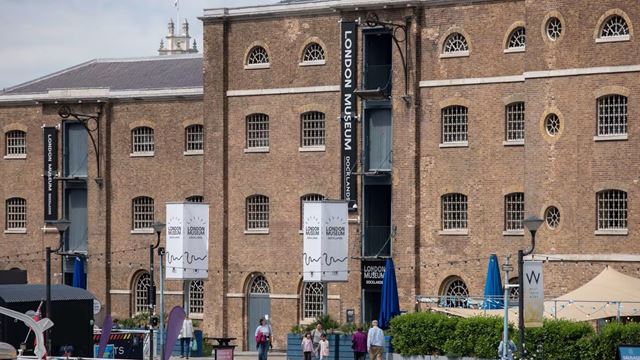 Visit the Museum of London Docklands. Credit: Museum of London Docklands. Image courtesy of Museum of London Docklands. Red-brick facade of the Museum of London Docklands with tourists walking past the entrance.