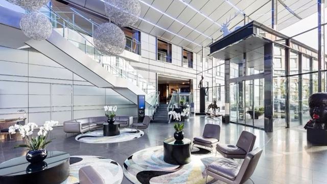Radisson Blu Hotel, London Canary Wharf East. Credit: Radisson Blu Hotels. Image courtesy of Radisson Blu Hotels. Sleek Radisson Blu Hotel lobby in Canary Wharf, east London, complete with glass doors and windows, grey seats and black tables with white flowers.