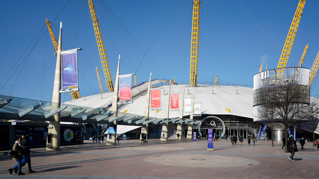 The exterior of the O2 Arena in London on a sunny day with people walking in the foreground.