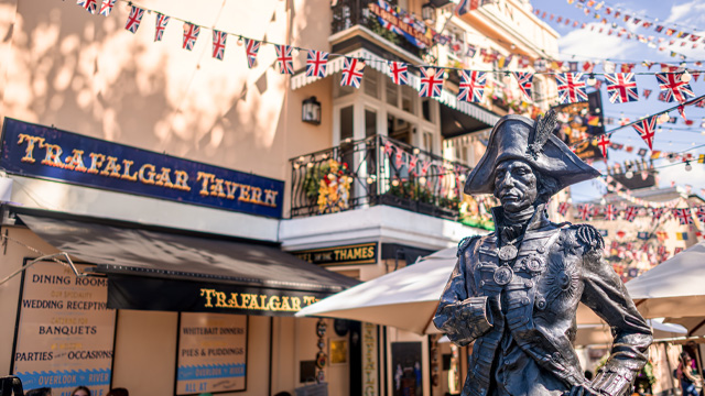 A statue of Lord Nelson with a traditional British pub with Union Jack bunting in the background.