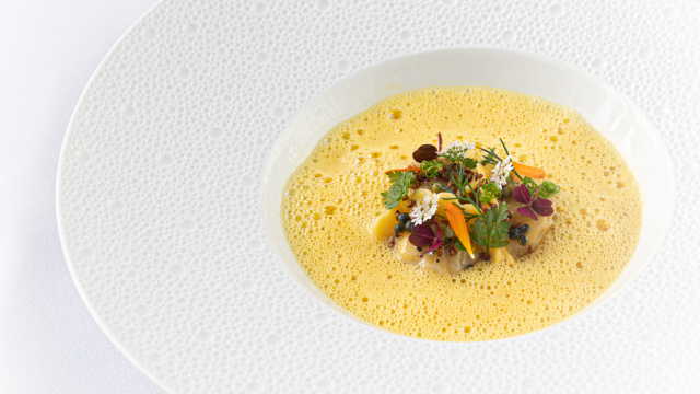 Close up of a dish with vegetables and an emulsion in a white plate on a table with white tablecloth.
