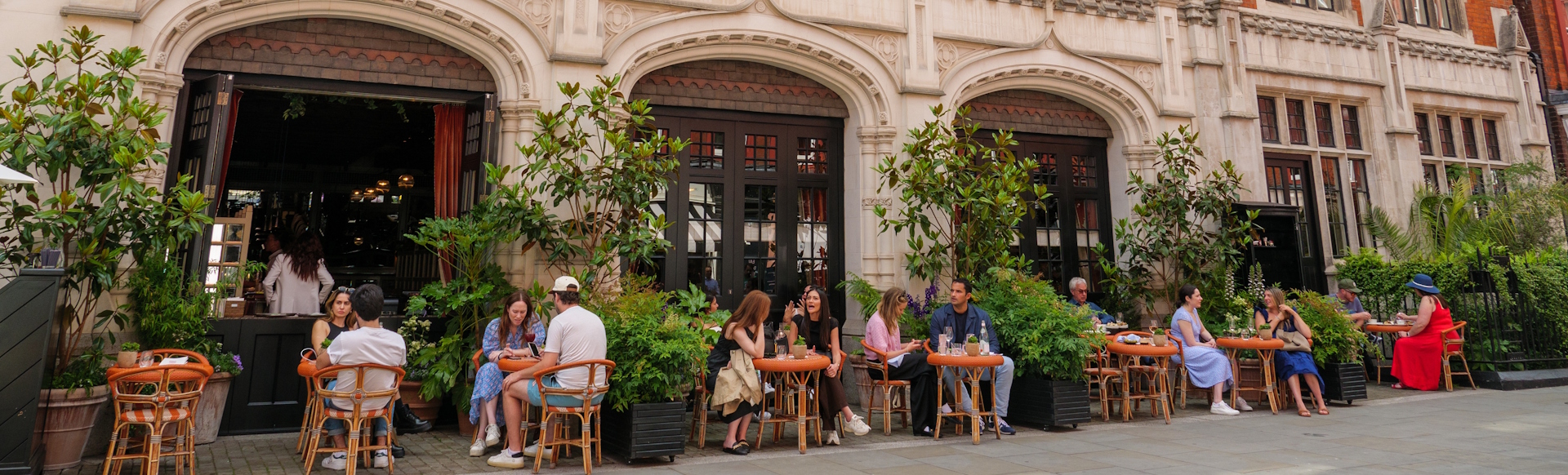 People sitting at outside tables outside Chiltern Firehouse restaurant building on a summer's day.