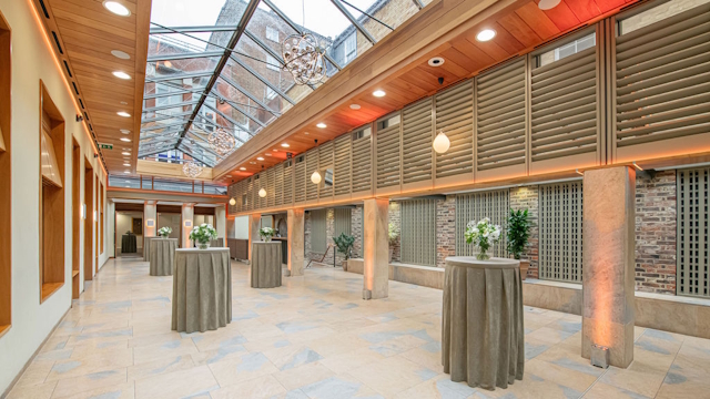 Book an event at No. 11 Cavendish Square. Credit: Susannah Fields. Image courtesy of No. 11 Cavendish Square. Bright event space with small round tables with flowers, glass roof and beige hues throughout.