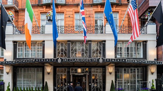 The front entrance of an elegant, classic hotel with four flag masts and a sign that reads Claridge's
