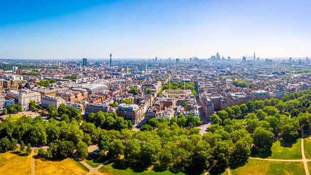 A wide angle aerial view of a central London neighbourhood with a large park at the foreground and the city skyline in the background.