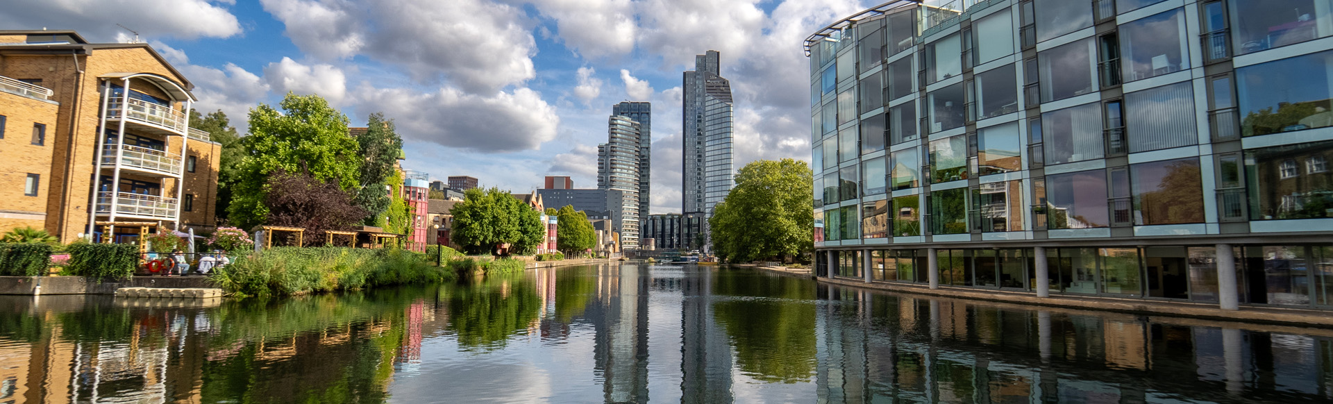 A daytime view of a canal on a sunny day with blue skies surrounded by modern residential and office buildings.