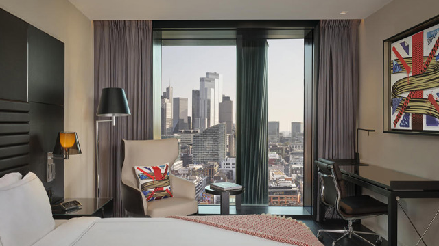 An interior of a modern hotel room with a window overlooking the city of London.