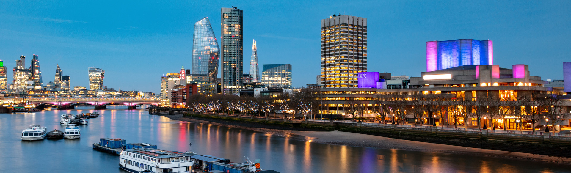 An evening view of the river Thames with illuminated buildings on the South Bank.