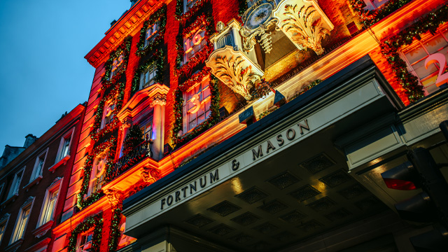 An evening view of the main entrance of Fortnum & Mason illuminated with Christmas lights.