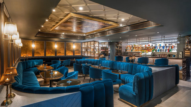 A contemporary, brightly lit interior of a hotel bar with blue seating.