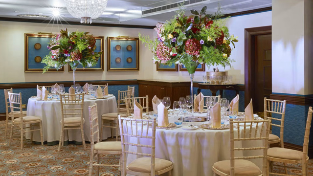Interior of a contemporary, smart restaurant with round tables draped with white tablecloths and decorative trees.
