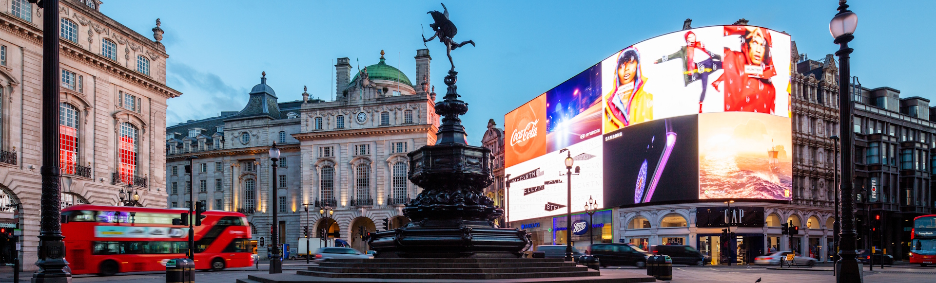 Eros statue and advertising screens at Piccadilly Circus in London's West End, with iconic red London bus driving past.