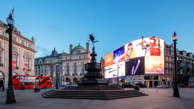 Eros statue and advertising screens at Piccadilly Circus in London's West End, with iconic red London bus driving past.