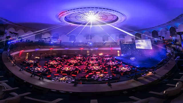 Host an event inside Church House Westminster. Credit: Church House Westminster. Image courtesy of Church House Westminster. Auditorium filled with people in attendance with red seats and blue and white lights.