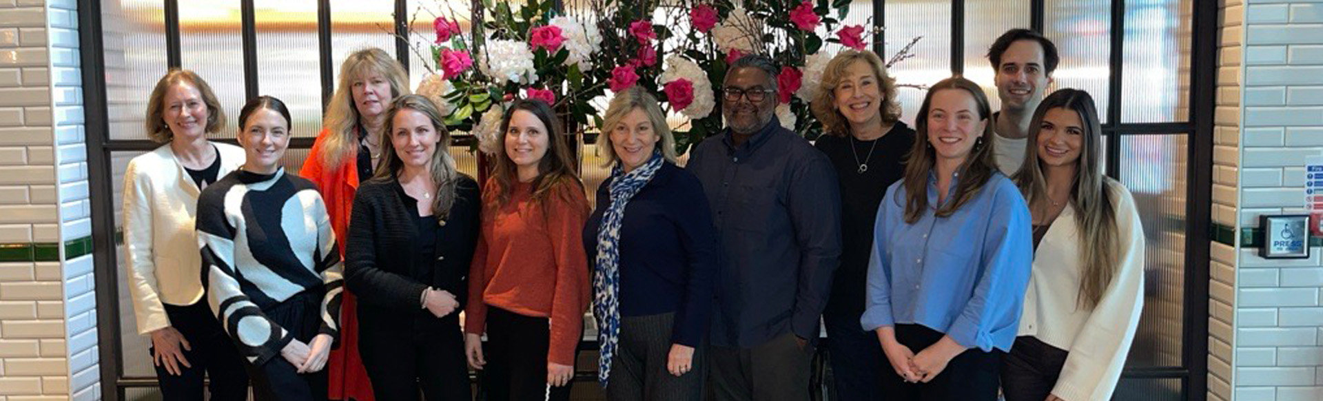 A group of people in business attire smiling at the camera with a floral tree in the background.