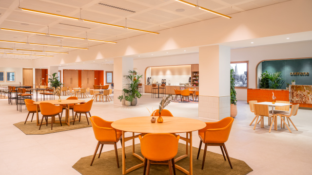 A brightly lit, modern dining area with round wooden tables and decorated in neutral tones. 