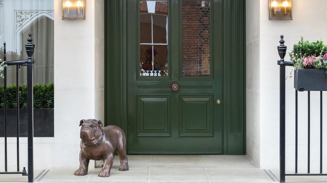 Exterior of Holmes Hotel London, featuring a dark green door, white walls and a small dog statue.