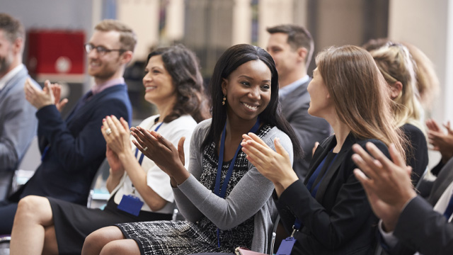 An audience of people smiling in business attire applauding a stage that is out of the frame.