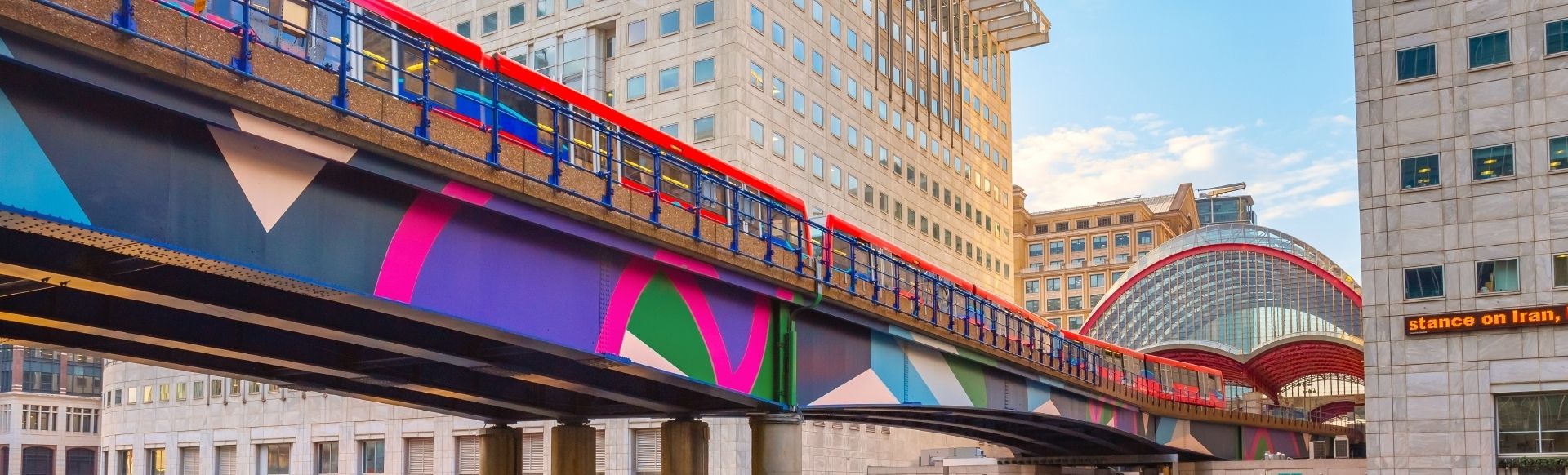 Canary Wharf, London. Image courtesy of cowardlion/Shutterstock. A DLR train on top of a colourful bridge at Canary Wharf DLR station in London.