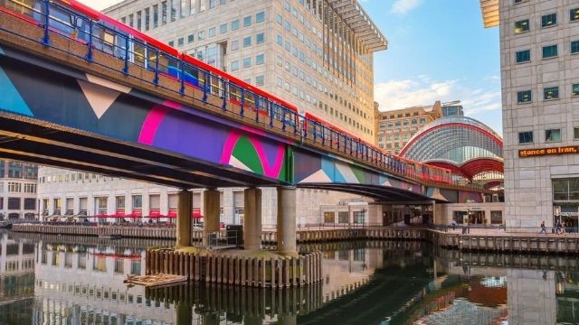 A DLR train on top of a colourful bridge at Canary Wharf DLR station in London.