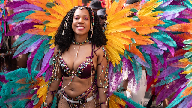 Woman smiling and dressed up with colourful orange green and purple feathers at the Notting Hill Carnival.