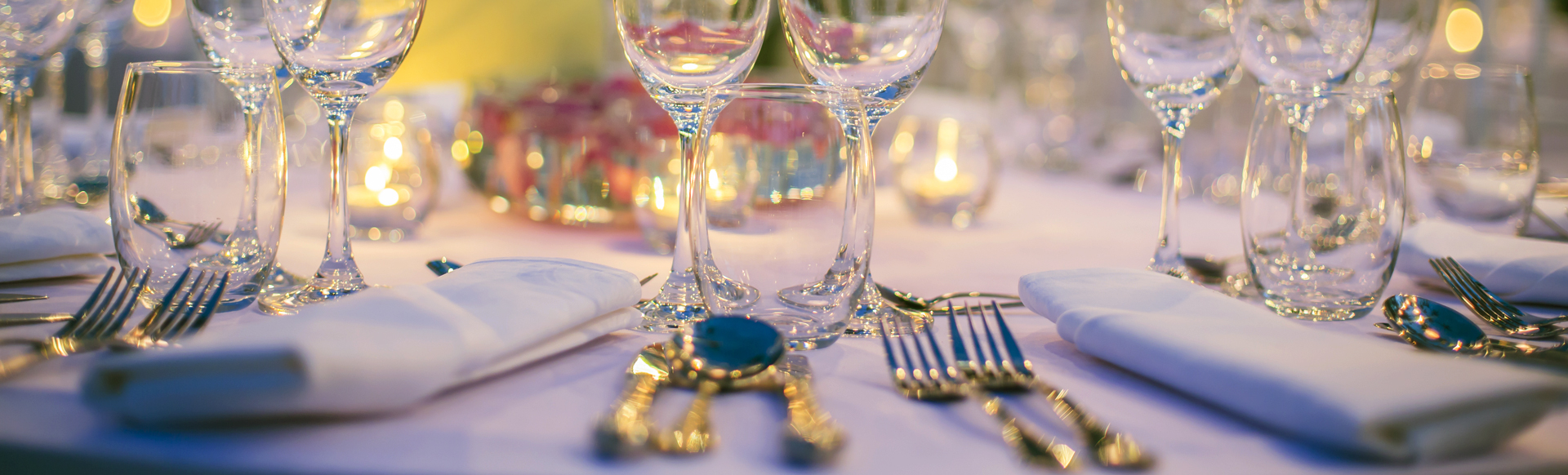 Dinner table close-up, with wine glasses, cutlery and candle lights placed in an elegant setting.