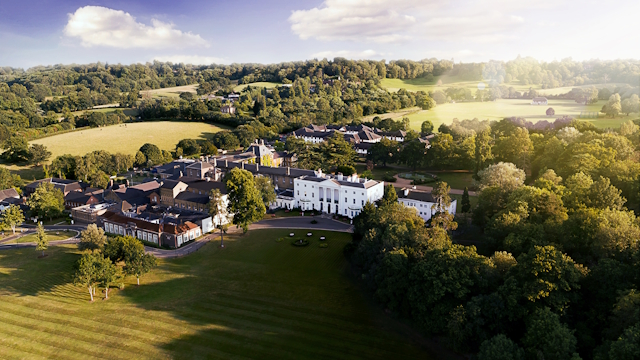 Aerial view of the De Vere Beaumont Hotel surrounded by trees and green space on a sunny day.