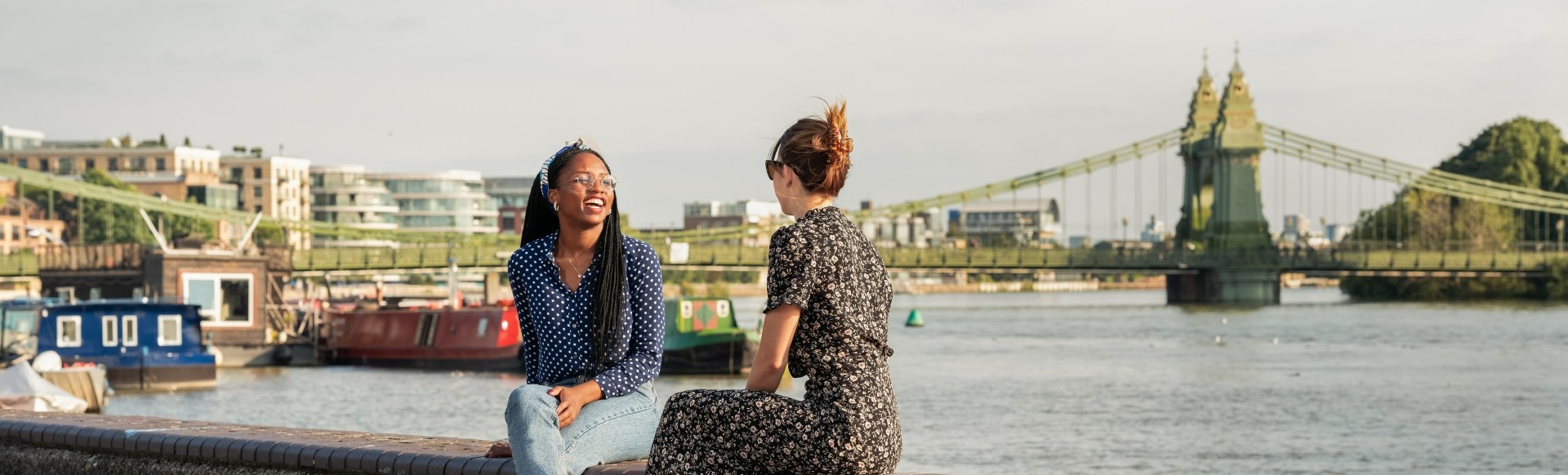 Two people chat while sitting on a ledge overlooking the river Thames in Hammersmith