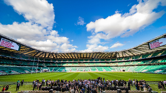 A daytime image of Twickenham Stadium playing field with a group of people in the foreground.