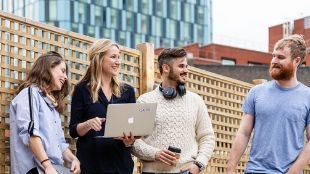 Two women and two men laughing and talking with their laptops in their hands