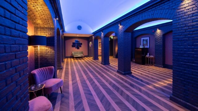 Open venue space at Grubstreet Author with purple chairs, a striped floor and blue brick walls.